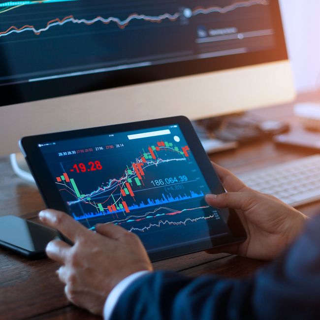 Businessman Checking Stock Market On Digital Tablet And A Desktop Computer With Stock Exchange Graph On Screen. Financial Stock Market. Analyzing Data In Office Background.