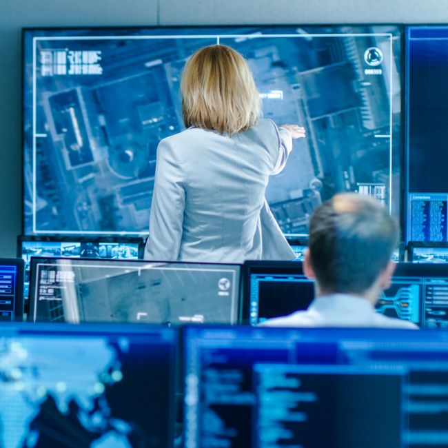 In The Government Surveillance Facility Team Of Officers Organize Interception Plan With Help Of Satellite Navigation. Big Screen Shows Top Down Images Of The Target.