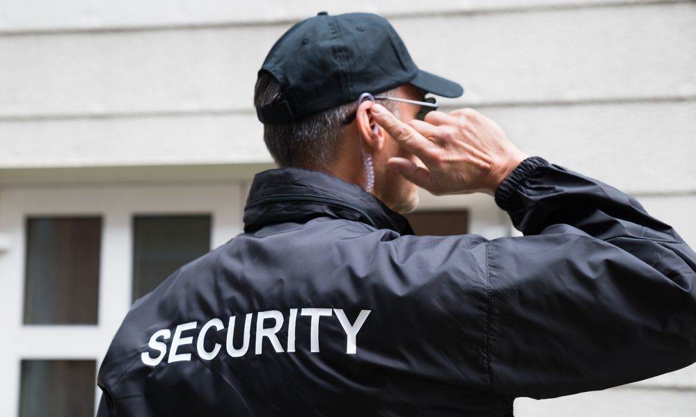 Security Guard Listening To Earpiece Against Building