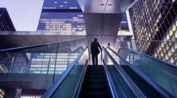 Businessman On Top Of Moving Escalator At Modern Illuminated Business District