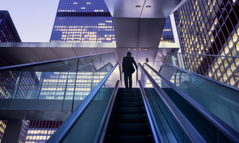 Businessman On Top Of Moving Escalator At Modern Illuminated Business District